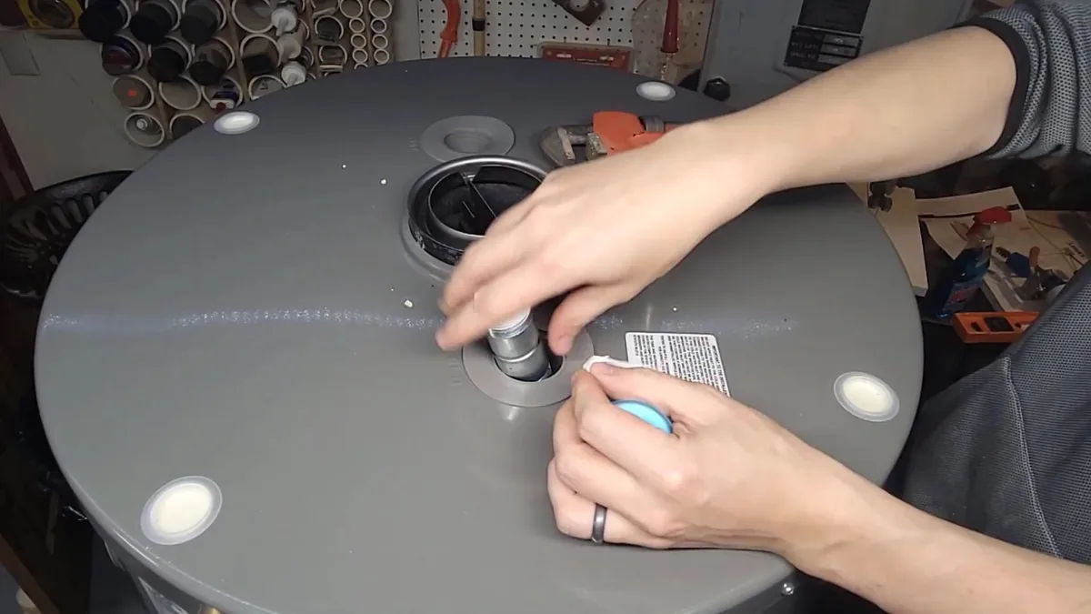Hands working at a fitting on the round top of a gray tank water heater