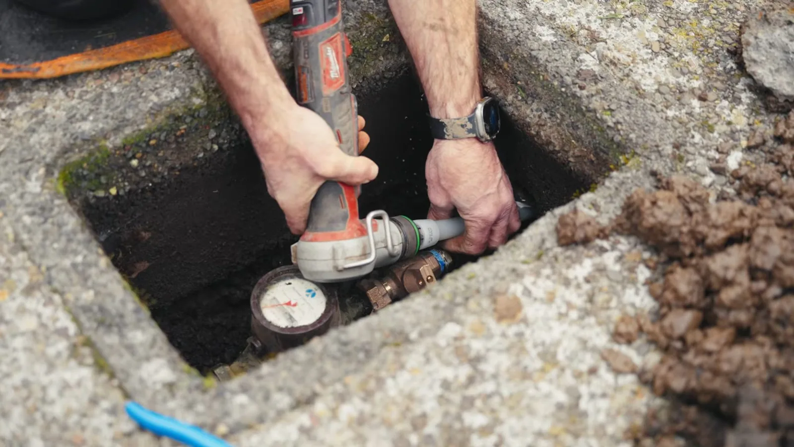 Hands holding a power tool at a water meter inside a concrete meter box
